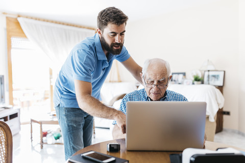 Erwachsener Enkel bringt seinem Großvater den Umgang mit dem Laptop bei, lizenzfreies Stockfoto