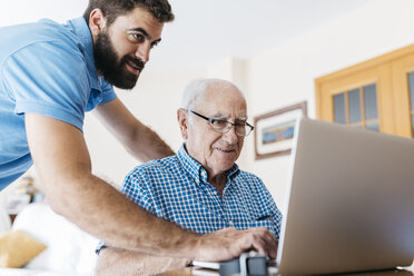 Adult grandson teaching his grandfather to use laptop - JRFF01416