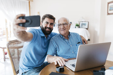 Portrait of adult grandson and his grandfather taking selfie with smartphone at home - JRFF01421