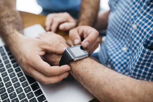 Adult grandson teaching his grandfather to use smartwatch, close-up - JRFF01422