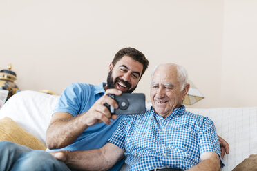 Portrait of adult grandson and his grandfather taking selfie with smartphone at home - JRFF01429