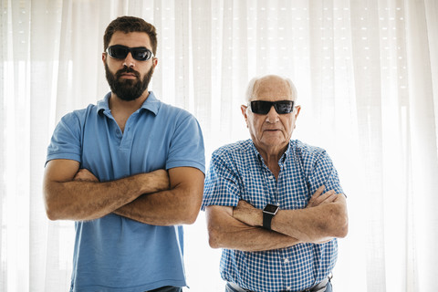 Porträt eines erwachsenen Enkels und seines Großvaters mit Sonnenbrille zu Hause, lizenzfreies Stockfoto