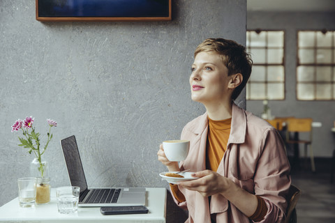 Frau mit ihrem Laptop genießt eine Tasse Kaffee in einem Café, lizenzfreies Stockfoto
