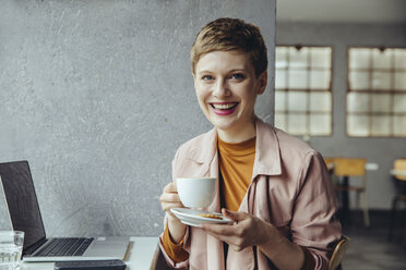 Porträt einer lächelnden Frau in einem Café mit Laptop und einer Tasse Kaffee - MFF03827