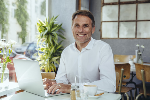 Porträt eines lächelnden Geschäftsmannes, der in einem Café mit Laptop arbeitet, lizenzfreies Stockfoto