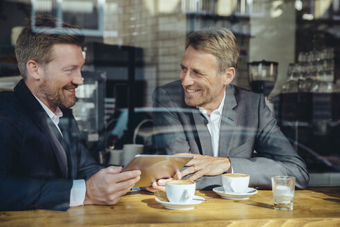 Zwei lächelnde Geschäftsleute mit Tablet in einem Cafe - MFF03865