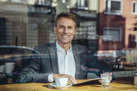 Porträt eines lächelnden Geschäftsmannes mit Tablet in einem Cafe, lizenzfreies Stockfoto