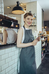 Portrait of smiling waitress holding menu in a cafe - MFF03873