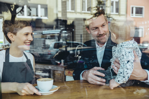 Waitress serving coffee to smiling customer with baby in cafe stock photo