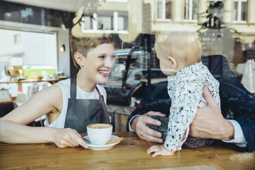 Kellnerin serviert Kaffee an lächelnden Kunden mit Baby im Café - MFF03878