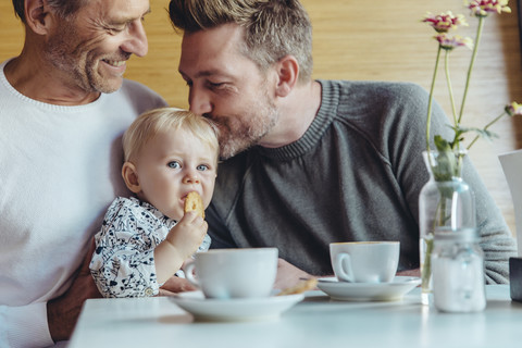 Homosexuelles Paar kuschelt mit seinem Baby im Cafe, lizenzfreies Stockfoto