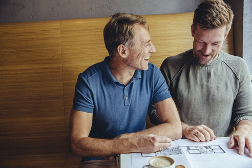 Ein glückliches schwules Paar betrachtet die Baupläne für sein Haus im Café - MFF03894