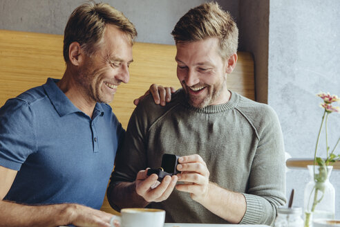 Excited gay couple with wedding ring in cafe - MFF03896