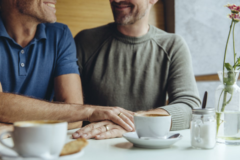 Gay couple putting their hands together with wedding rings in cafe stock photo