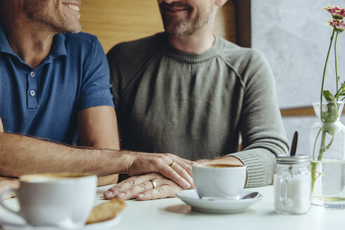 Homosexuelles Paar, das sich in einem Café die Hände mit Eheringen reicht - MFF03903