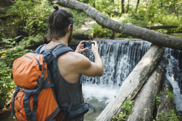 Young man taking a cell phone picture at a waterfall in forest - VPIF00030