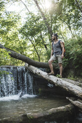 Junger Mann steht auf einem Baumstamm an einem Wasserfall im Wald - VPIF00032
