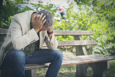 Man with head in his hands sitting on park bench - JUNF00890