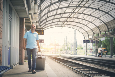 Lächelnder Mann mit Gepäck auf dem Bahnsteig - JUNF00892