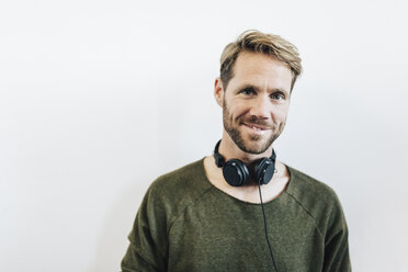 Porträt eines lächelnden Mannes mit Kopfhörern vor weißem Hintergrund - GIOF03164