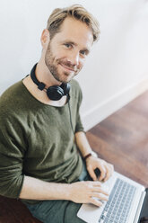 Porträt eines lächelnden Mannes mit Kopfhörern und Laptop - GIOF03165