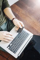 Man sitting on the floor paying online with credit card, partial view - GIOF03167