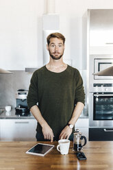 Porträt eines in der Küche stehenden Mannes, der die Augenbrauen hochzieht - GIOF03169