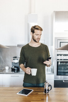 Porträt eines Mannes, der in der Küche steht und auf sein Mobiltelefon schaut - GIOF03170
