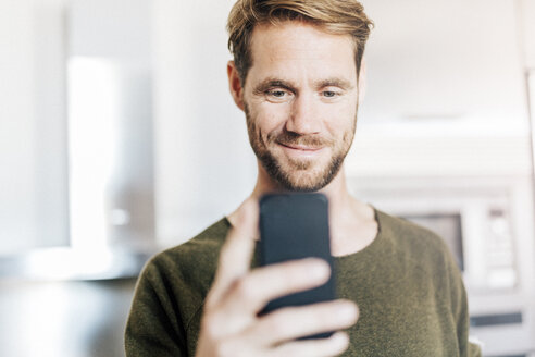 Porträt eines lächelnden Mannes, der auf sein Mobiltelefon schaut - GIOF03172