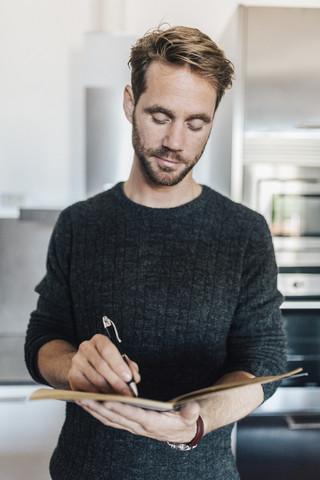 Porträt eines Mannes, der in der Küche in ein Notizbuch schreibt, lizenzfreies Stockfoto