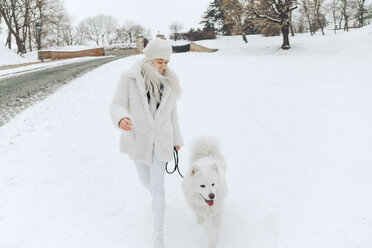 Junge Frau geht mit ihrem Hund im Schnee spazieren - ZEDF00824