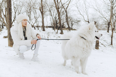 Weiß gekleidete junge Frau mit weißem Hund im Schnee, die etwas beobachtet - ZEDF00825