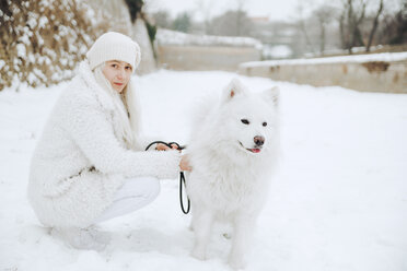 Porträt einer weiß gekleideten jungen Frau mit weißem Hund im Schnee - ZEDF00831