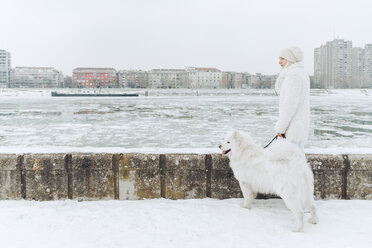 Serbien, Petrovaradin, weiß gekleidete junge Frau steht mit weißem Hund im Schnee am Flussufer - ZEDF00836
