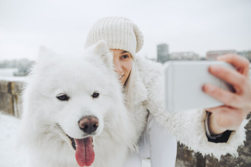 Serbien, Petrovaradin, weiß gekleidete Frau macht Selfie mit weißem Hund im Winter - ZEDF00837