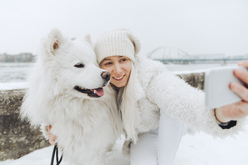 Weiß gekleidete Frau nimmt Selfie mit ihrem weißen Hund im Winter - ZEDF00838