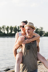 Young man giving girlfriend piggyback ride at the riverbank - UUF11535