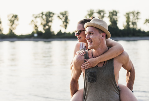 Young man giving girlfriend piggyback ride at the riverbank stock photo