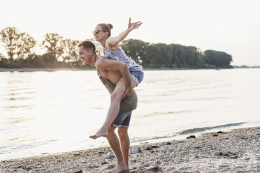 Young man giving girlfriend piggyback ride at the riverbank - UUF11538