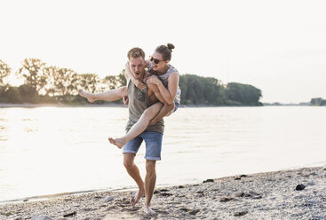 Young man giving girlfriend piggyback ride at the riverbank - UUF11539