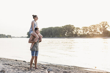 Young man carrying girlfriend on shoulders at the riverbank - UUF11540