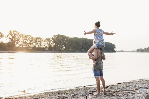 Junger Mann trägt Freundin auf den Schultern am Flussufer, lizenzfreies Stockfoto