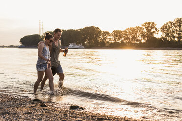 Happy young couple wading in river at sunset - UUF11546