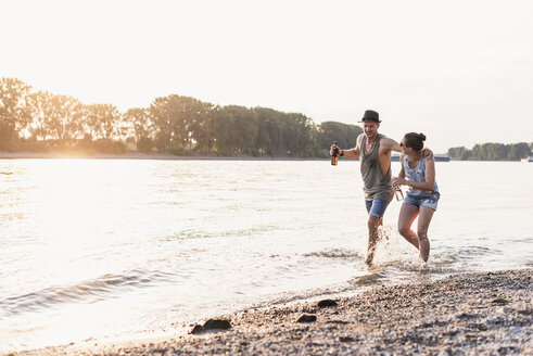 Happy young couple wading in river at sunset - UUF11547