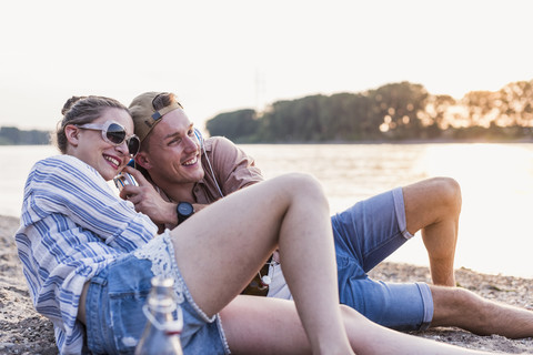 Junges Paar entspannt sich am Flussufer und teilt Kopfhörer, lizenzfreies Stockfoto