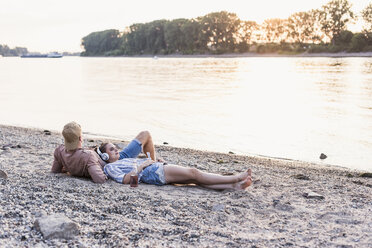 Junges Paar entspannt sich am Flussufer bei Sonnenuntergang - UUF11552