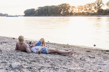 Young couple relaxing at the riverbank at sunset - UUF11552