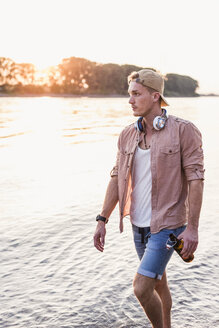 Young man walking at the riverbank at sunset - UUF11555