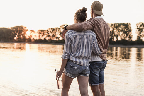 Young couple watching the sunset above a river - UUF11563