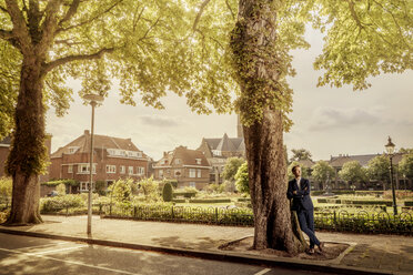 Niederlande, Venlo, Geschäftsmann lehnt an einem Baum - KNSF02412